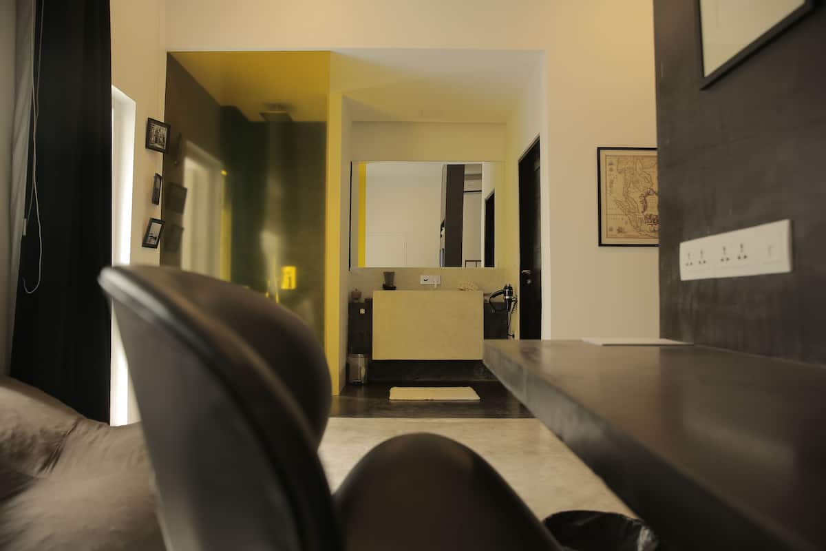 A modern hotel room with a dark leather sofa, a small kitchenette, and a large mirror.