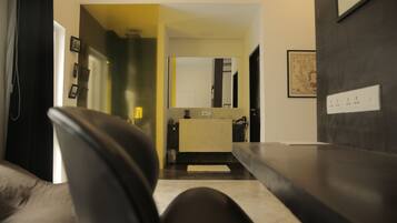 A modern hotel room with a dark leather sofa, a small kitchenette, and a large mirror.