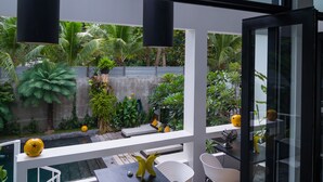 A modern interior with a dining area featuring a table and chairs, large windows, and a view of a lush garden. - Arthur&Paul - Caters to Men (Phnom Penh)