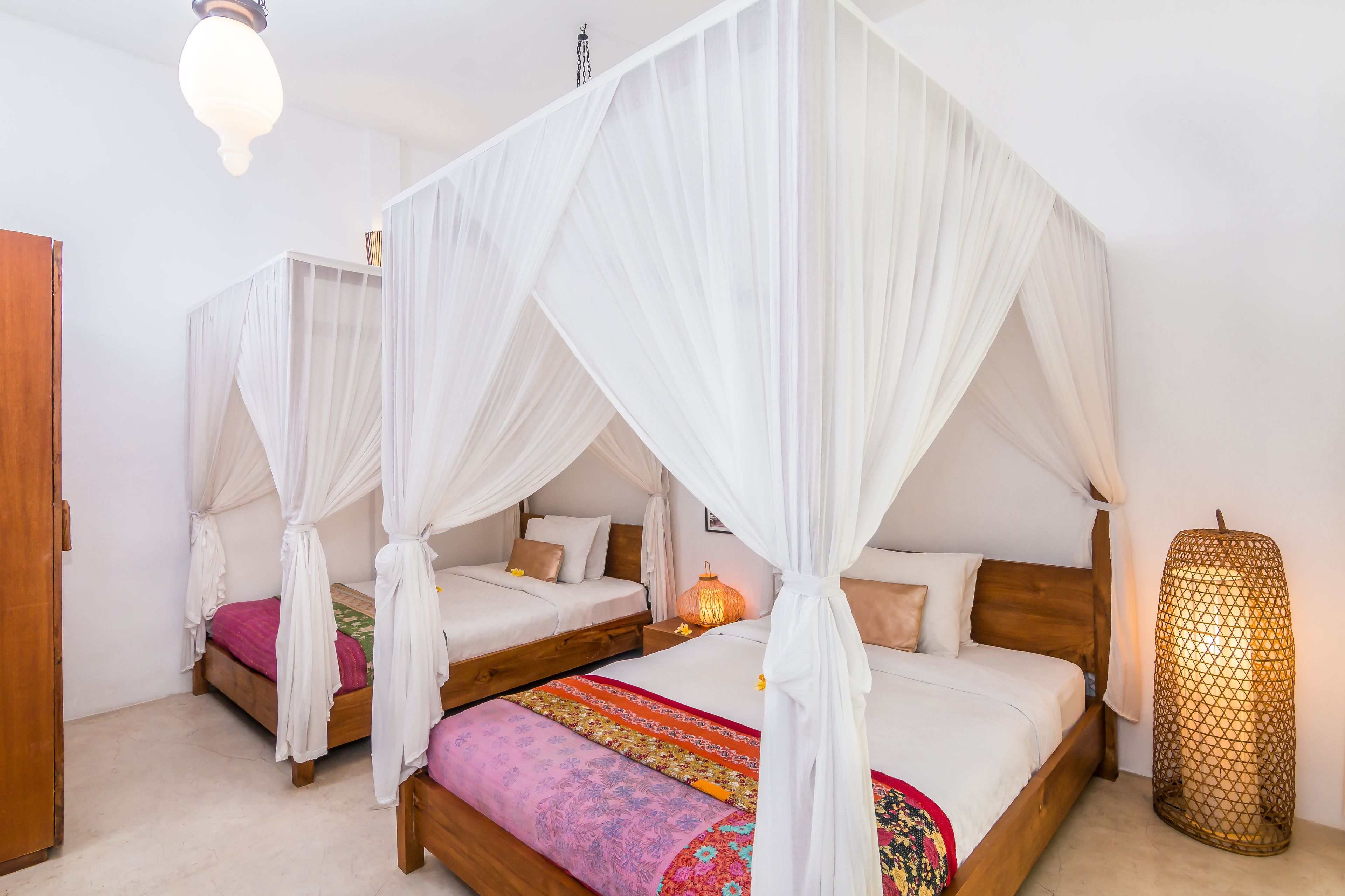 Una habitación con dos camas, cada una con dosel blanco, cabeceros de madera y ropa de cama colorida.