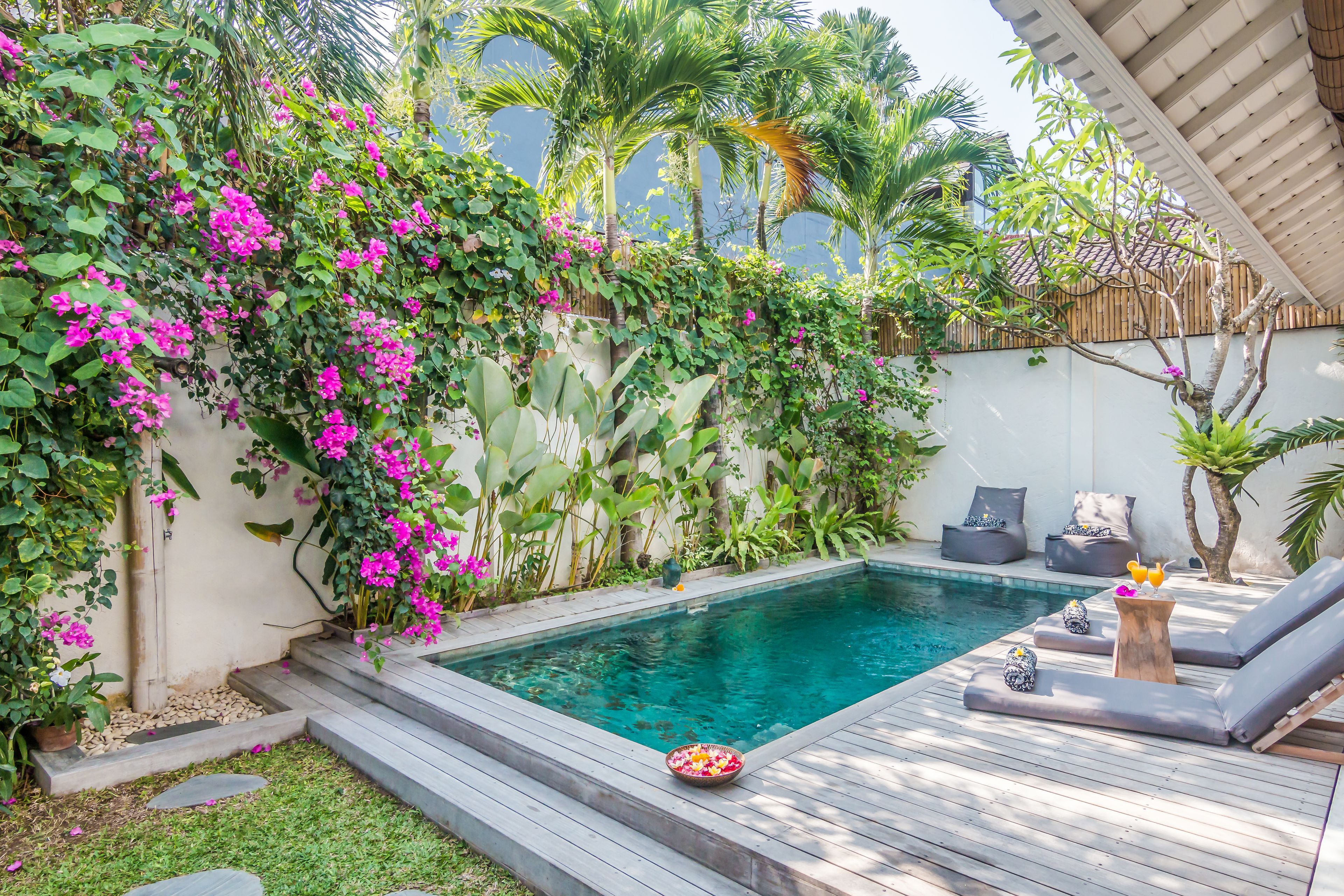 A poolside area with a wooden deck, lounge chairs, and a small table with a bowl of fruit.