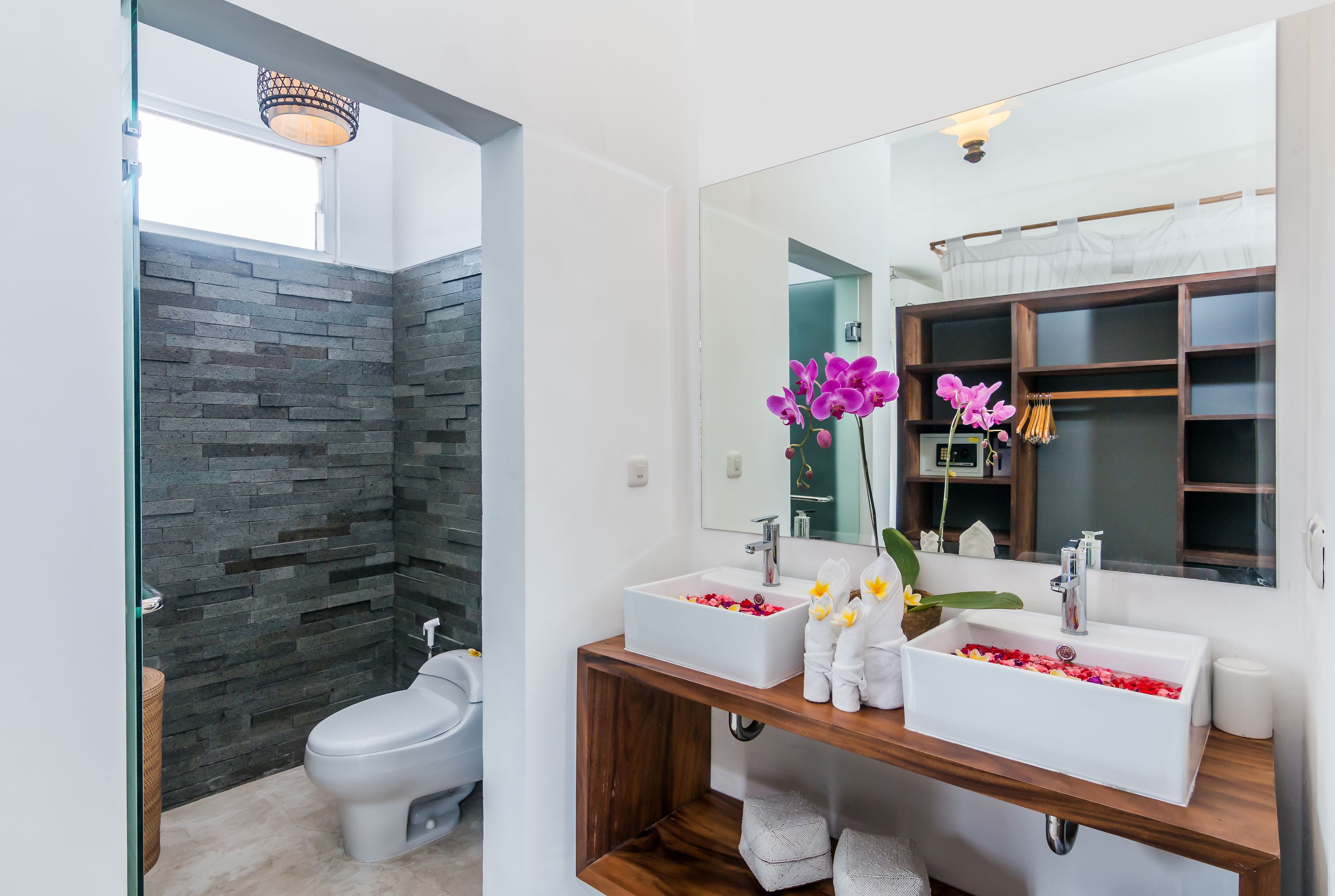 Un baño moderno con pared de piedra, dos lavamanos, un inodoro y un espejo.