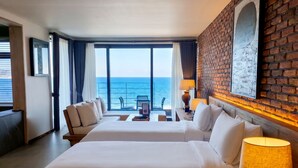 A hotel room with two beds, a balcony with a view of the sea, a brick accent wall, and a framed picture. - Zen Hideaway@Jeju (Seogwipo)