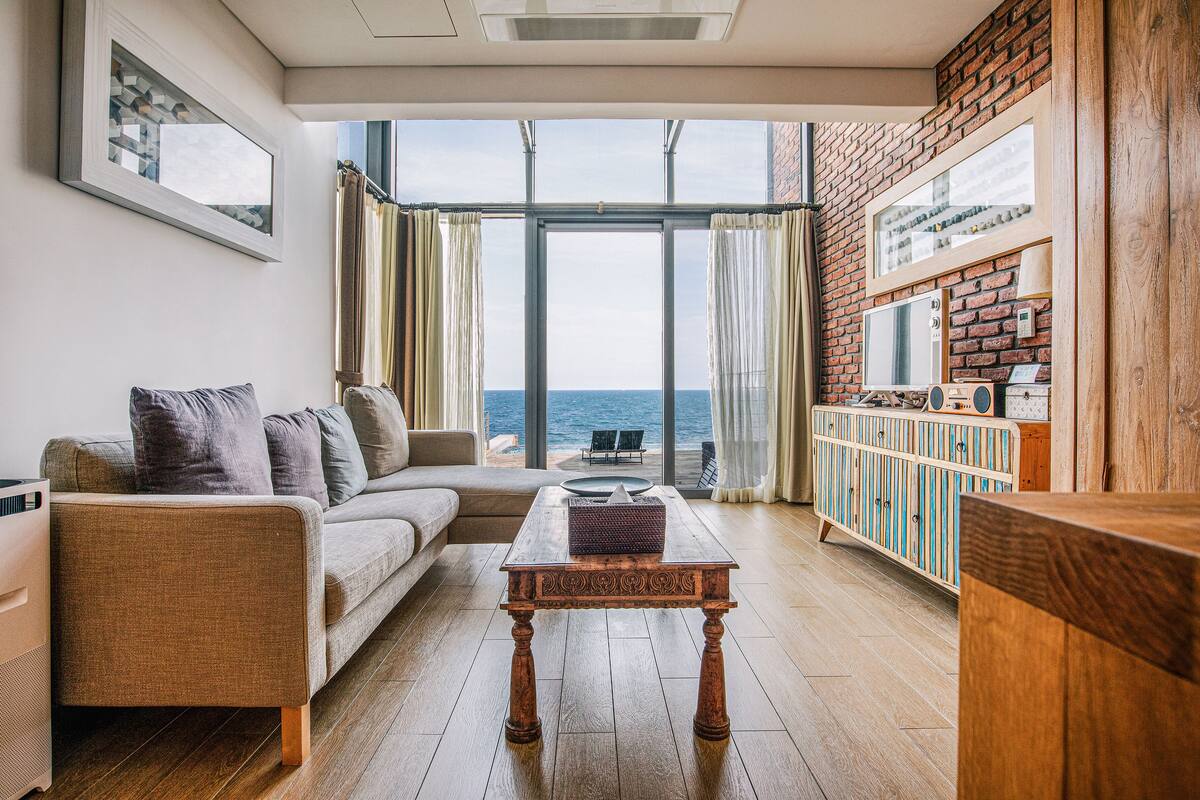 Un salon avec un canapé, une table basse et une vue sur la mer grâce à de grandes fenêtres.
