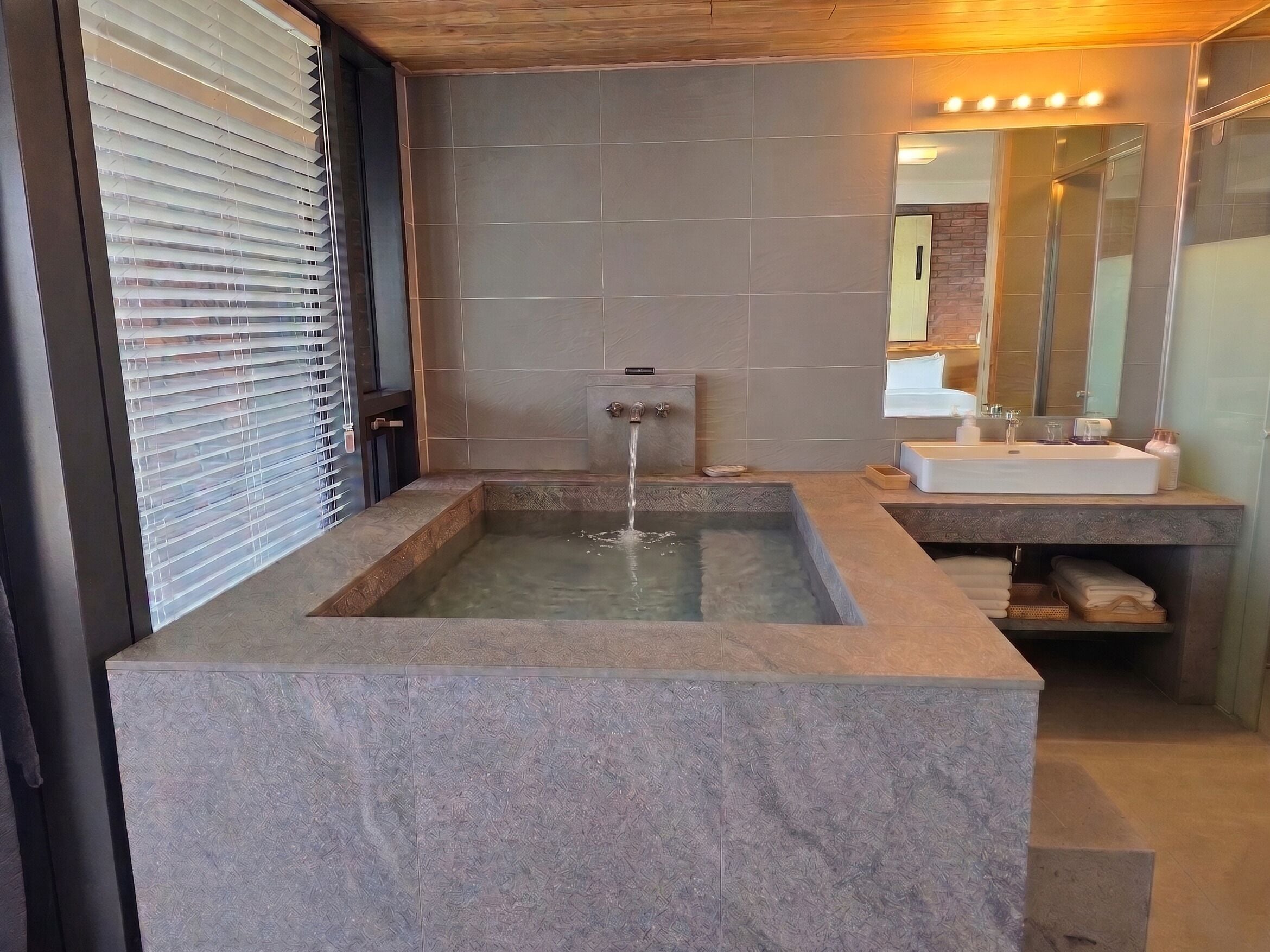 Un baño moderno con una bañera de piedra rectangular, un lavamanos y un espejo.