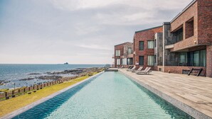 A poolside view with a clear view of the ocean, a wooden deck, and a brick building. - Zen Hideaway@Jeju (Seogwipo)