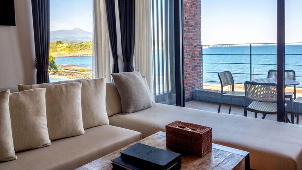 A modern hotel room with a sofa, a wooden table, and a view of the sea. - Zen Hideaway@Jeju (Seogwipo)