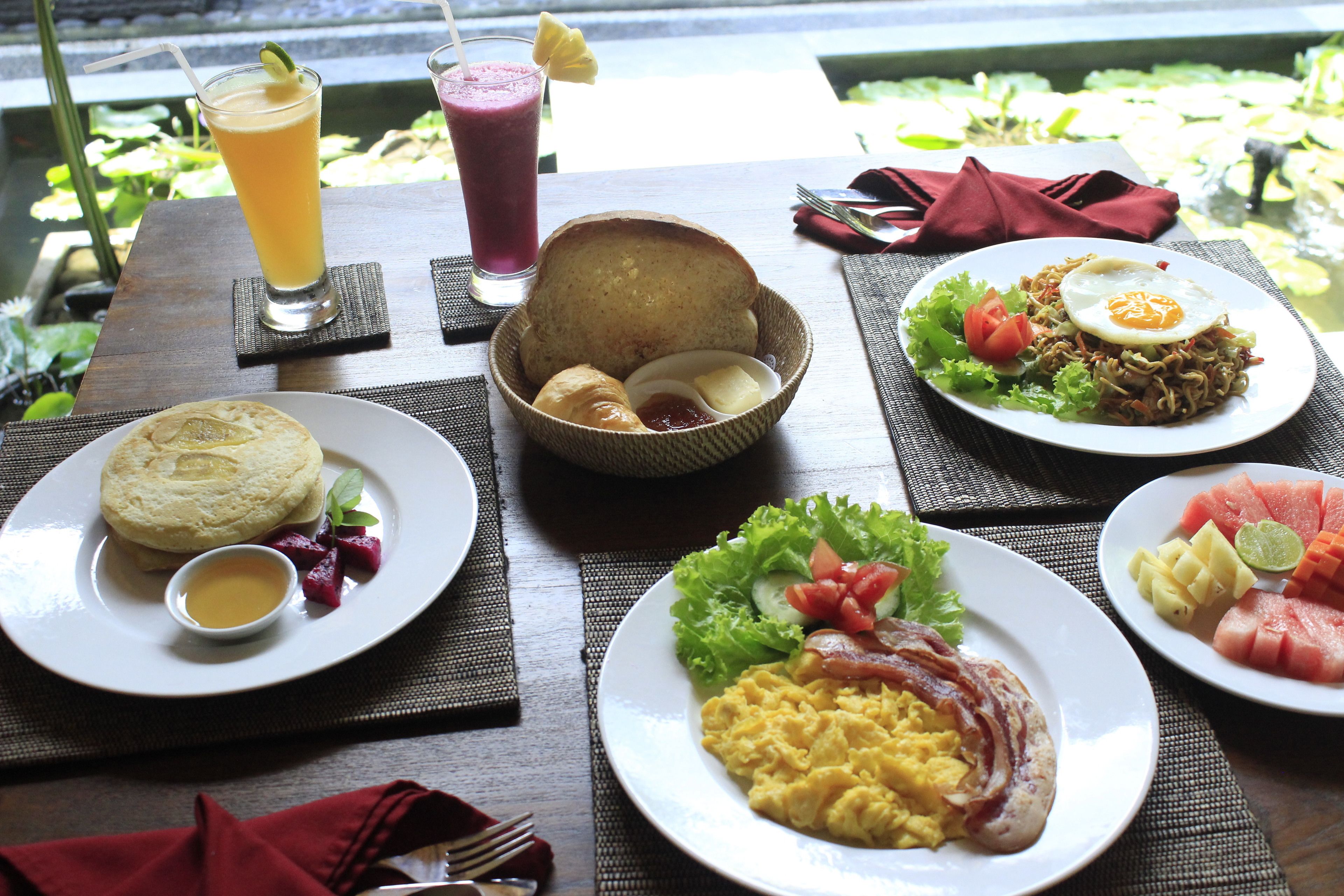 A table set with various breakfast dishes including eggs, bacon, and fresh fruit, along with two drinks.