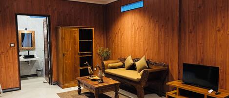 Una sala de estar con piso de madera, un sofá, una mesa de centro, un mueble para televisor, un ventilador de techo y un armario de madera.