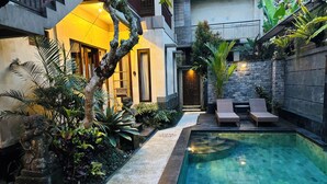 Un área de piscina moderna al aire libre con una pared de piedra, sillones de descanso y una escalera que lleva a un segundo nivel.