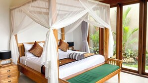 Una cama con dosel y cuatro columnas, con piecera verde, mesitas de noche de madera y una mesita auxiliar con lámpara.