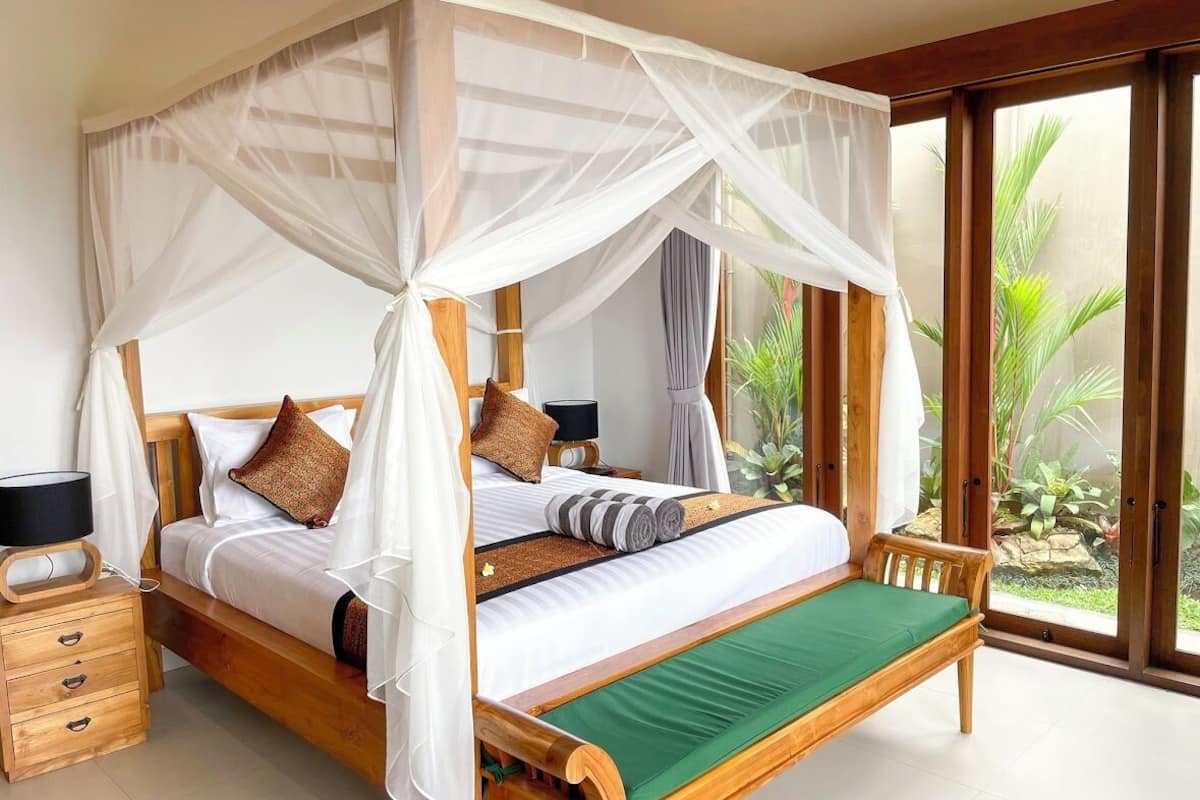 A four-poster canopy bed with a green footboard, wooden nightstands, and a bedside table with a lamp.