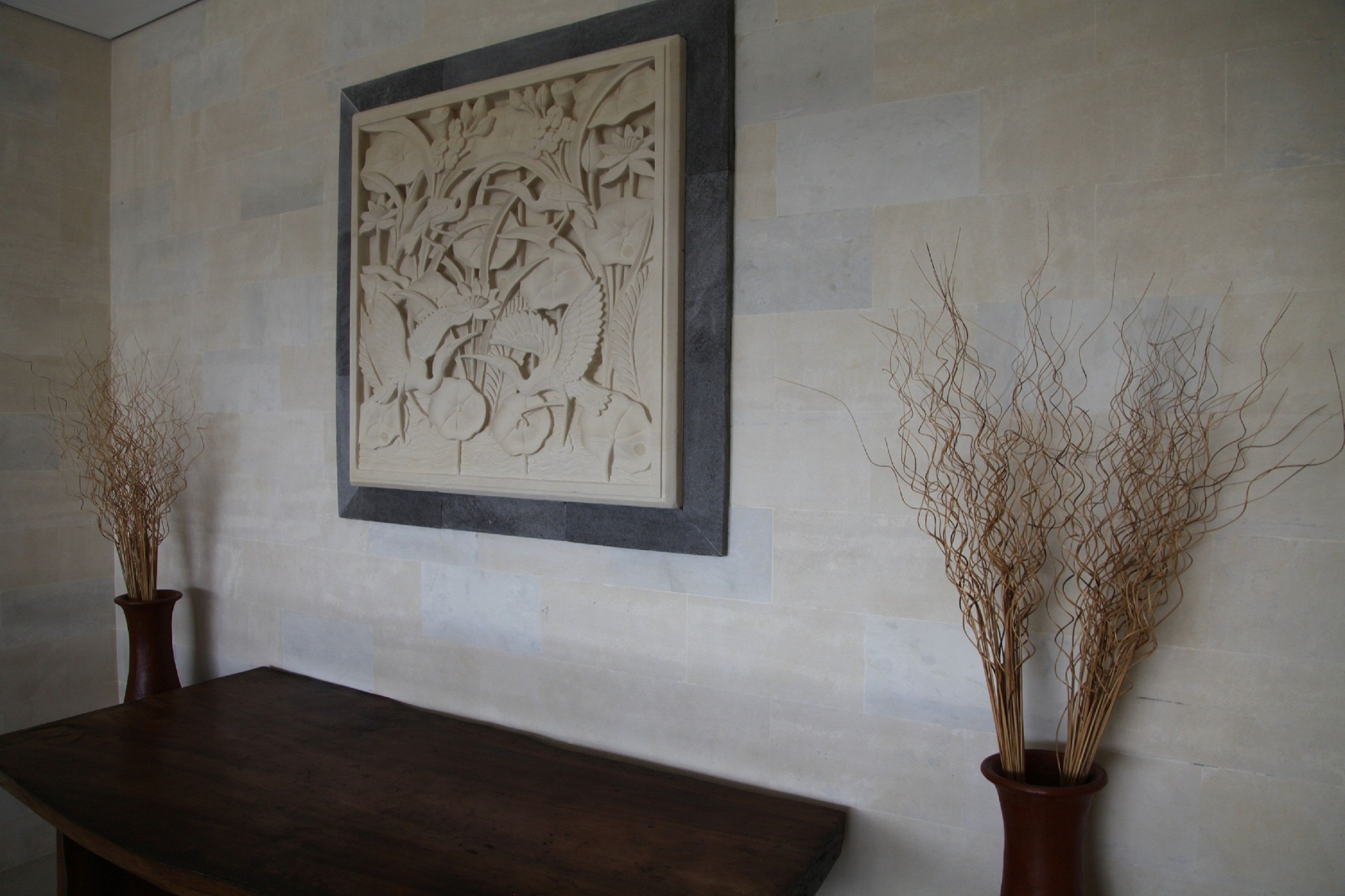 A wall with a carved panel and two vases with dried plants.