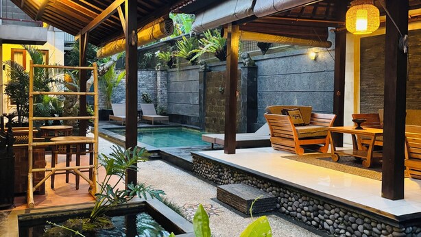 Zona de piscina con deck de madera, asientos y una pequeña fuente.