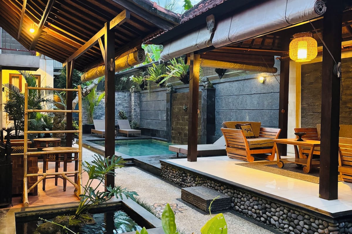 A pool area with a wooden deck, seating, and a small water feature.