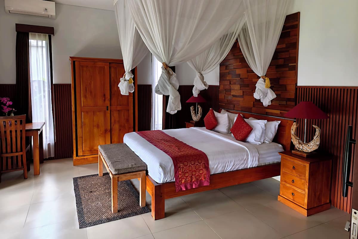 A bedroom with a wooden bed, a bench, a wardrobe, and a mosquito net.