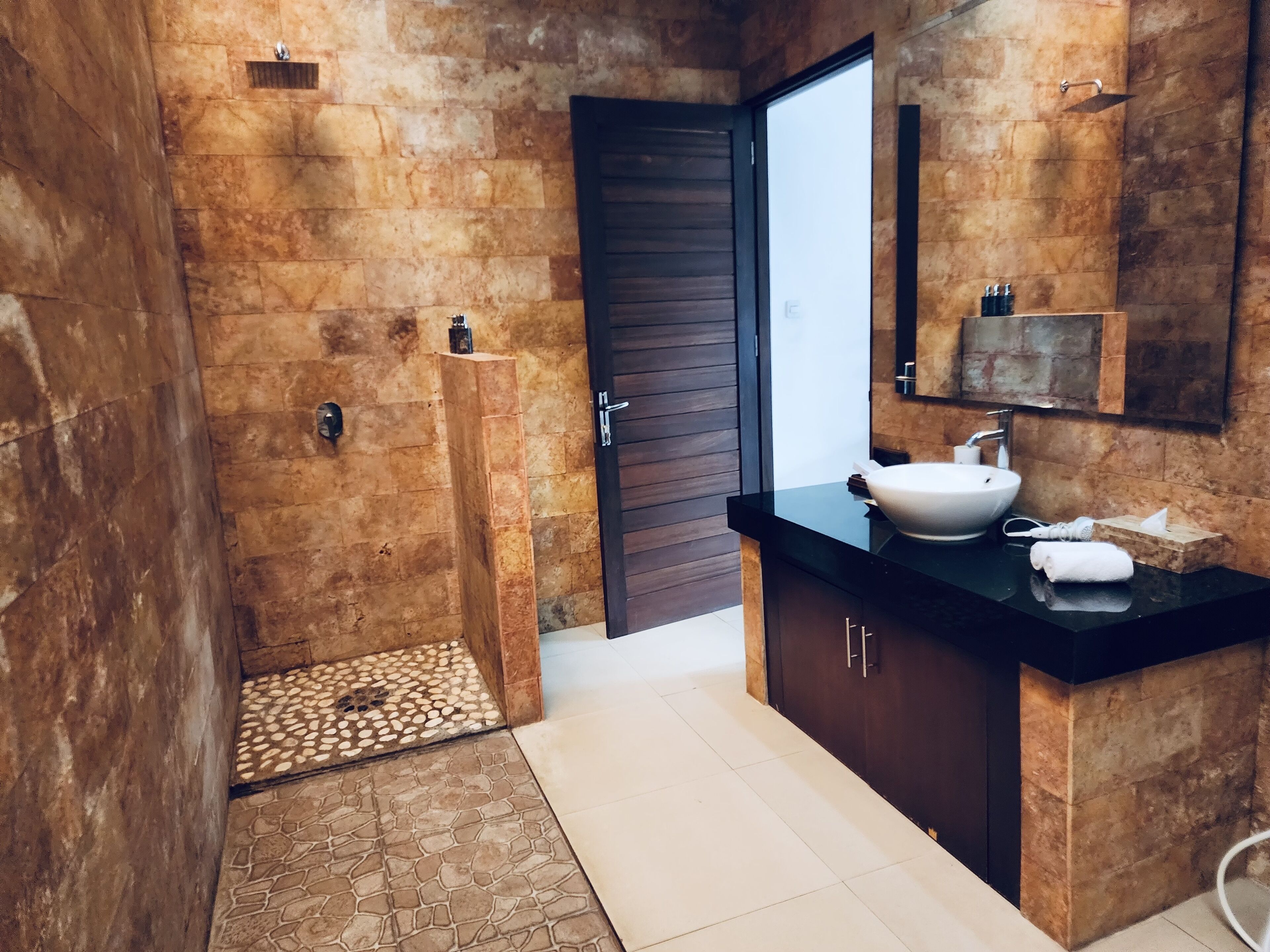 A bathroom with a stone wall, a wooden door, a white sink, and a mirror.