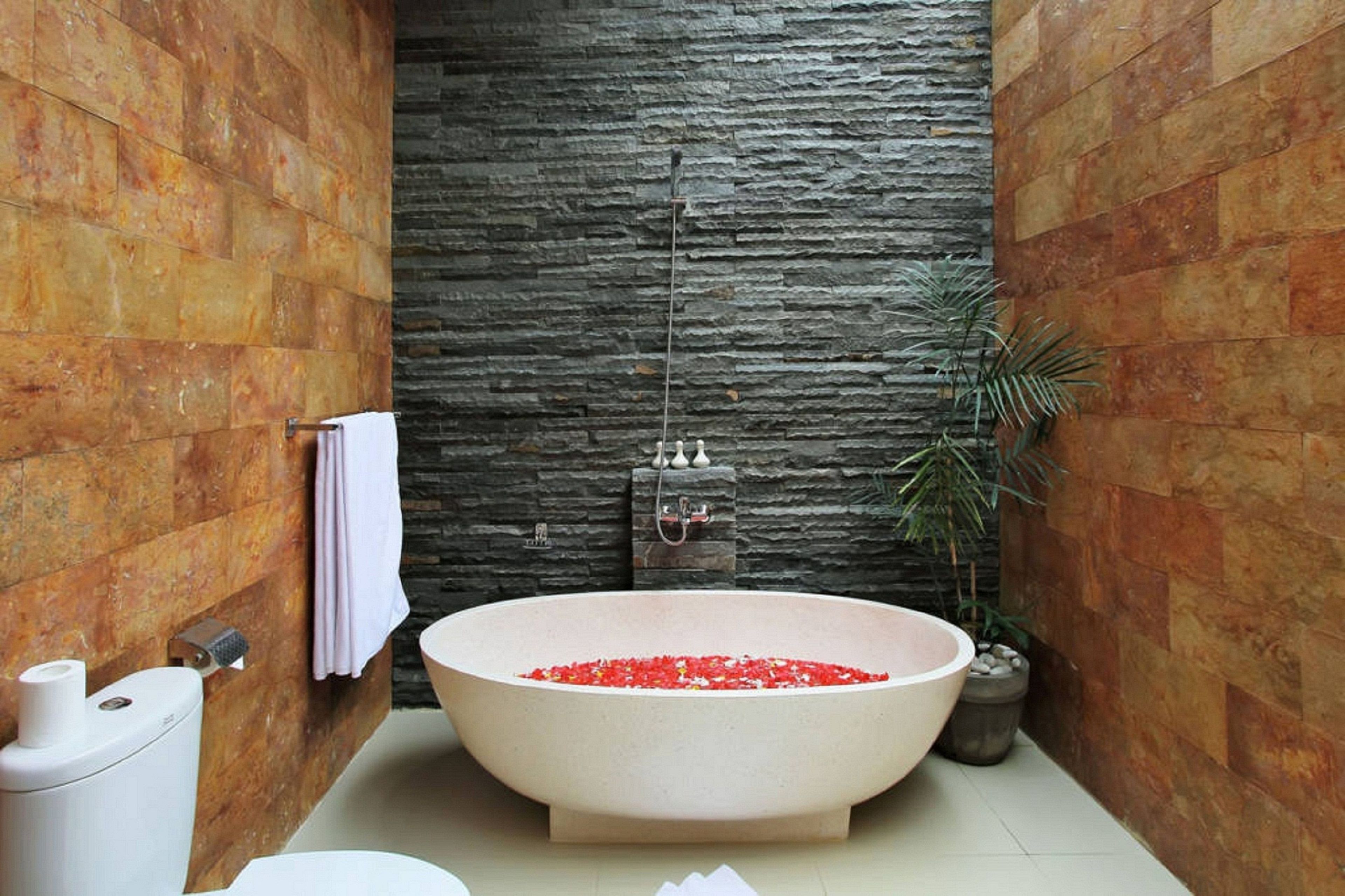 A bathroom with a freestanding bathtub filled with red bath salts, a toilet, and a sink.