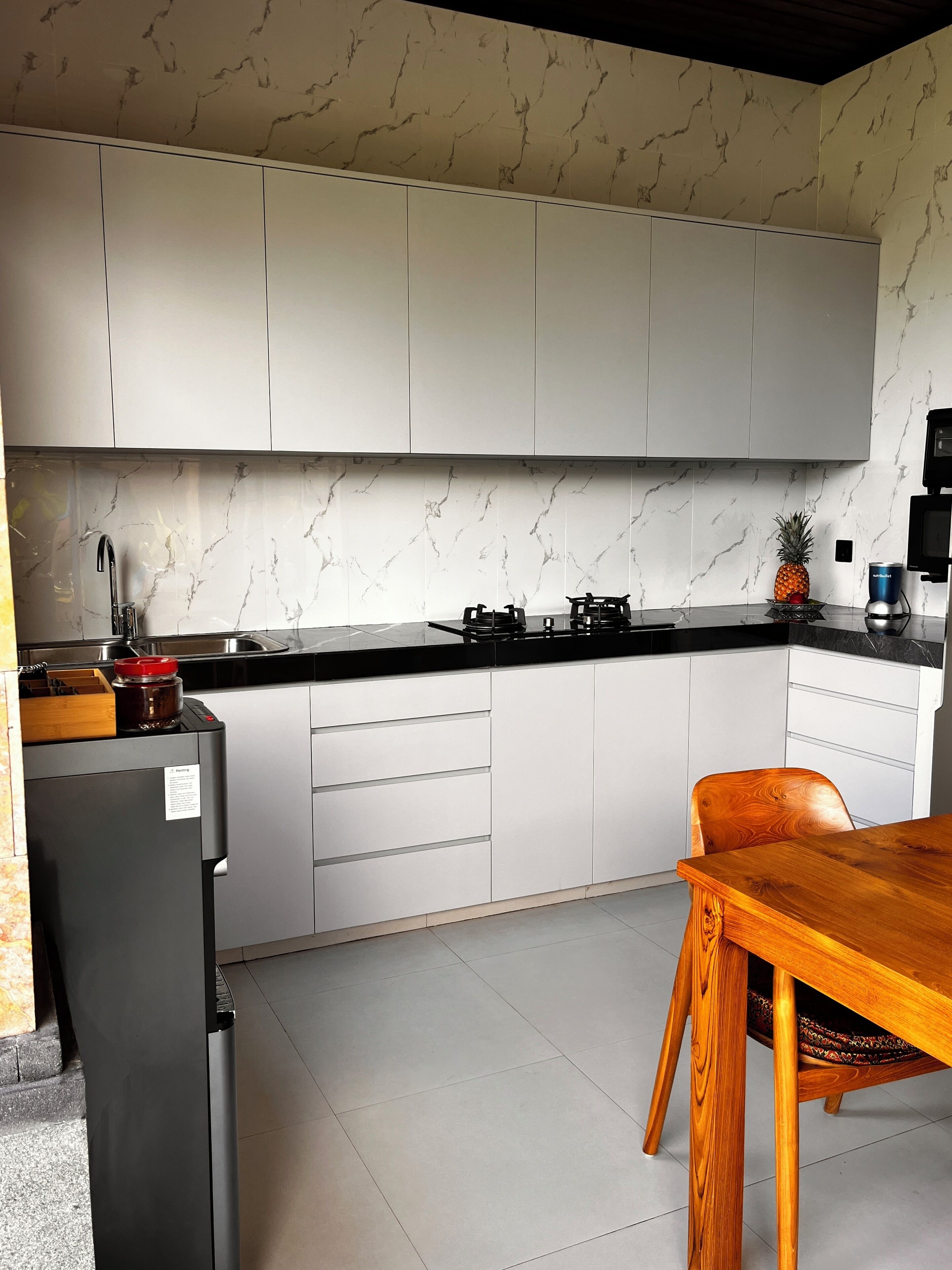 A modern kitchen with white cabinets, a black countertop, and a wooden dining table.