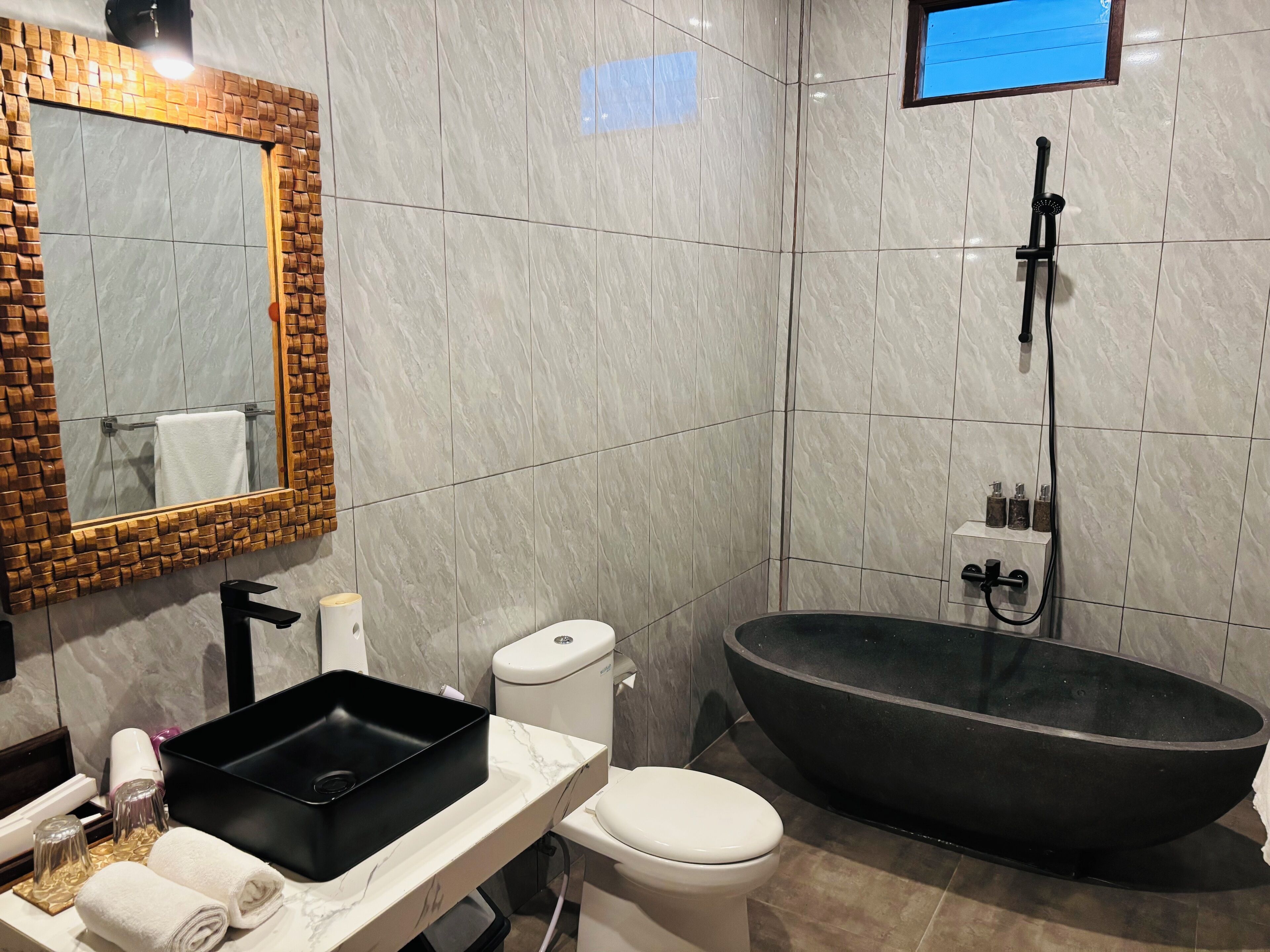 Un baño moderno con una bañera independiente negra, un inodoro blanco y un tocador de mármol con lavamanos negro.