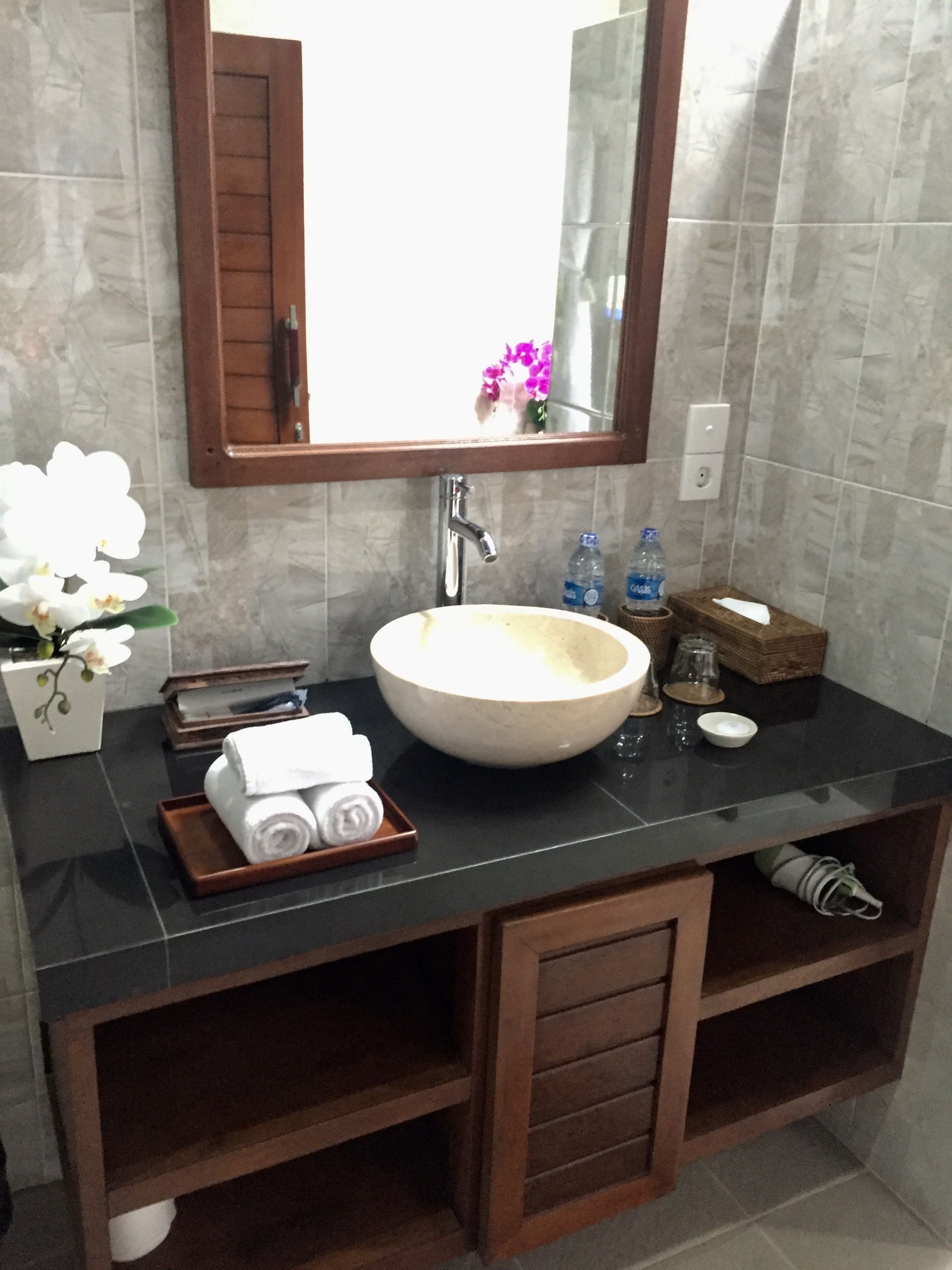 Un baño con un lavamanos grande, un espejo y un mueble de tocador de madera. Hay toallas y artículos de aseo en el mueble.