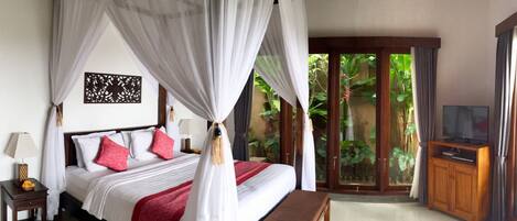 A bedroom with a four-poster bed, a wooden nightstand, a bedside table, a bench, a television on a wooden stand, and a view of greenery through a glass door.