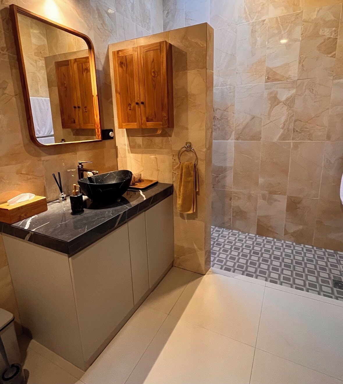 A modern bathroom with a black sink, wooden cabinets, a mirror, and tiled walls.