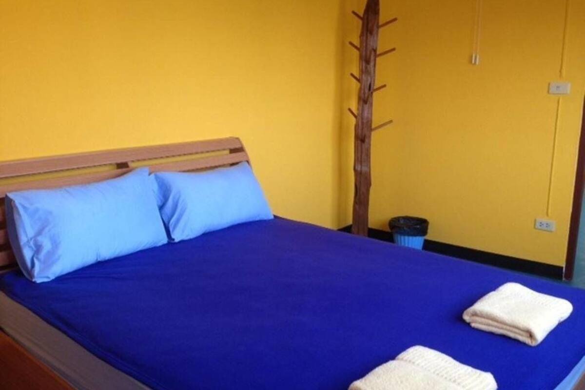 Una cama con colchón azul y dos almohadas, un cabecero de madera y una manta azul.