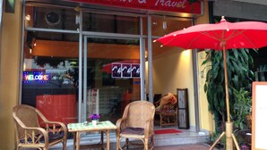 A restaurant named 'Chill Inn Tour & Travel' with wicker chairs and a red umbrella outside. - Just Chill Inn - Hostel (Chiang Mai)