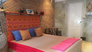 A bedroom with a brick-patterned headboard, a bed with red and beige bedding, and a small table with chairs. - Just Chill Inn - Hostel (Chiang Mai)