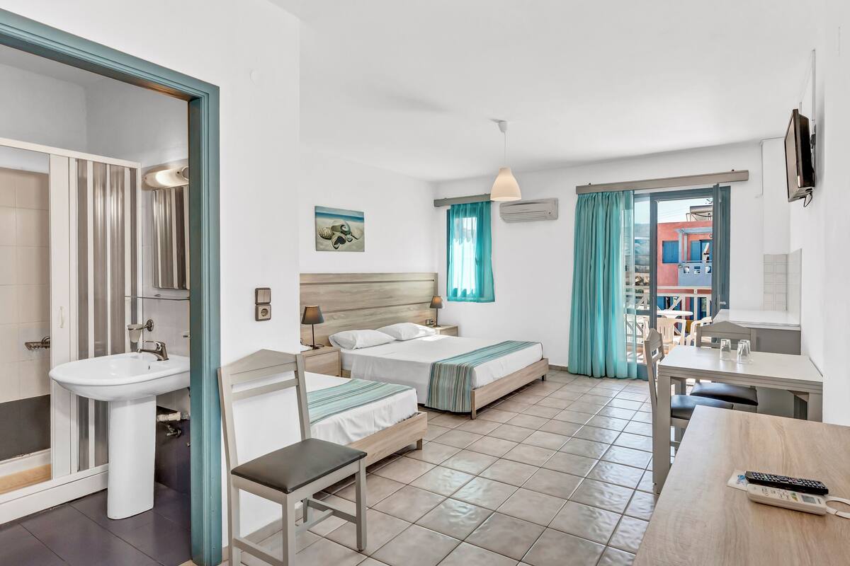 Habitación de hotel con cama, mesita de noche, silla, escritorio y baño con lavamanos.
