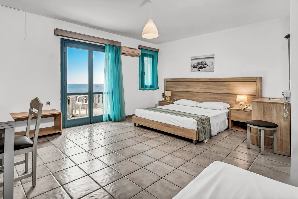 Habitación de hotel moderna con cama, escritorio, silla y vista al mar a través de un ventanal grande.