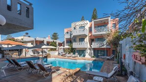 A pool area with lounge chairs and a clear blue pool surrounded by buildings. - Marilisa Hotel (Hersonissos)