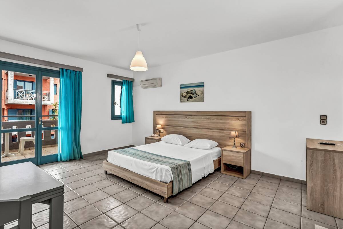 Una habitación de hotel con cama, mesitas de noche, un escritorio y vistas al balcón exterior.