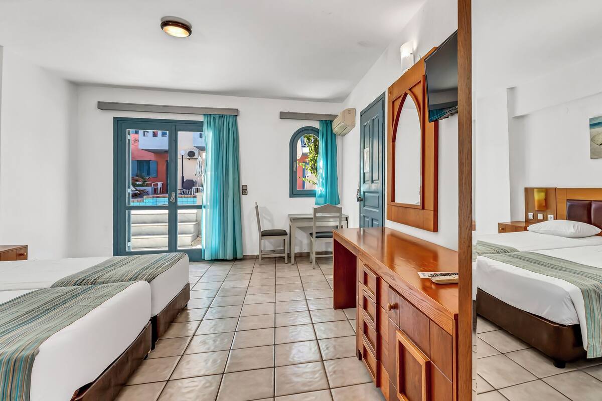Habitación de hotel con dos camas, un escritorio y una silla. Tiene una ventana con cortinas, una puerta y vistas al exterior.