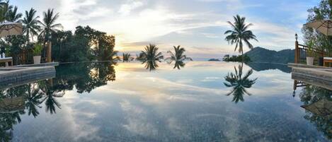 A clear view of a swimming pool with a tiled floor, surrounded by palm trees and a mountainous landscape in the background.