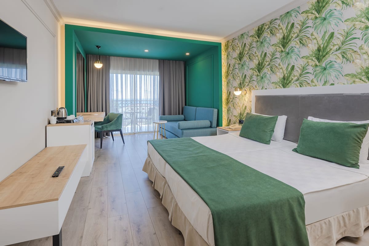 A hotel room with a bed, a desk, a chair, a balcony, and a view of the outdoors.
