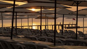 A beachside lounge area with rows of sun loungers and umbrellas, overlooking a body of water and a pier. - L'Oceanica Beach Resort Hotel - All Inclusive (Kemer)