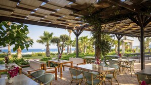 An outdoor patio with wooden tables and chairs, surrounded by greenery and palm trees, overlooking a scenic view. - L'Oceanica Beach Resort Hotel - All Inclusive (Kemer)