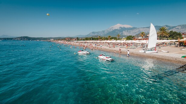 A beach with clear blue water, boats, and a sailboat. - L'Oceanica Beach Resort Hotel - All Inclusive (Kemer)
