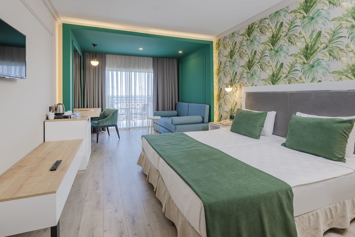 A hotel room with a bed, a desk, a chair, a balcony, and a view of the outdoors.