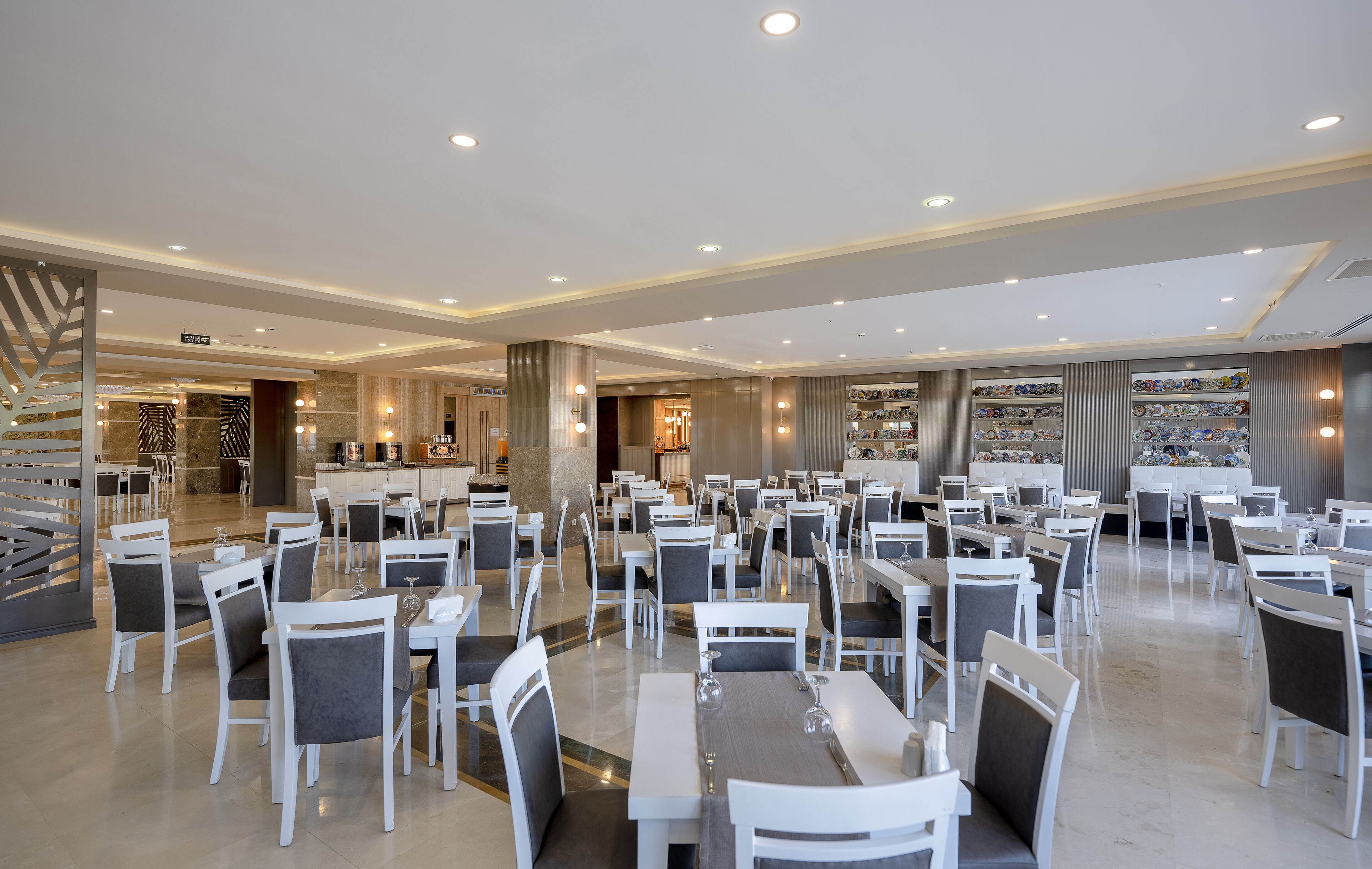 A spacious dining area with multiple tables and chairs, a central bar area, and a well-lit ceiling with recessed lighting.
