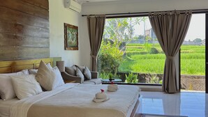 Un dormitorio con una cama grande, cabecera de madera, un cuadro y vista a un campo verde por la ventana.