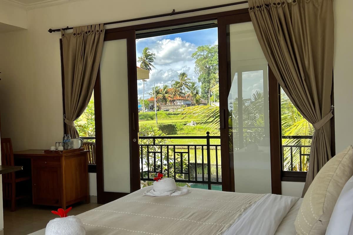 A hotel room with a large bed, a desk, and a view of a lush garden through the sliding glass doors.
