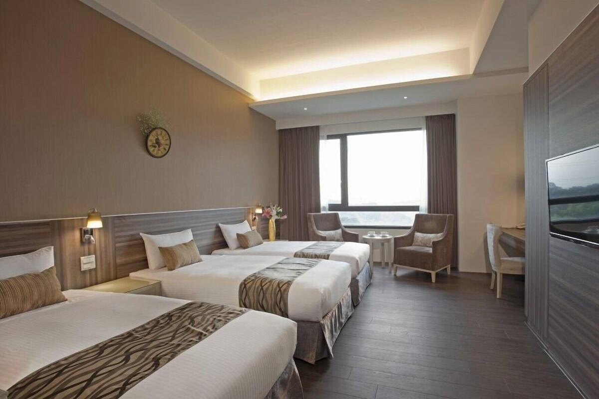 A hotel room with three beds, a TV, a desk, and a view of the outdoors.