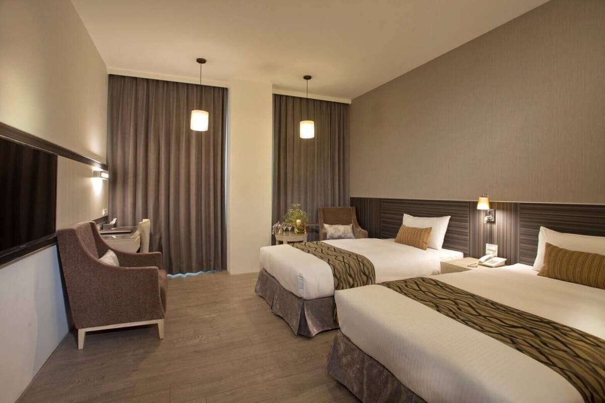 A hotel room with two beds, a desk, a chair, and a large mirror.