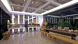 Un interior moderno con suelo de madera, una mesa larga con bancos y una exhibición de diversos objetos, incluyendo zapatos y cerámica.