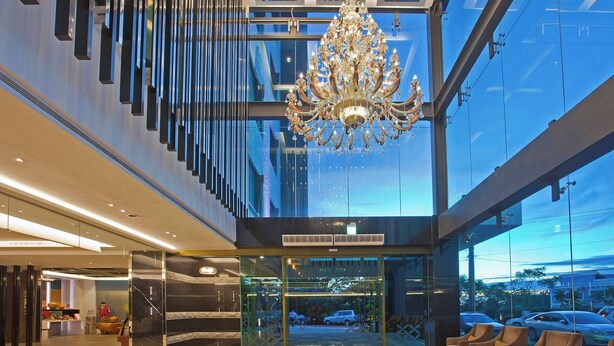 Un moderno vestíbulo de hotel con una imponente lámpara de araña, un ascensor de cristal y una zona de estar con sillones.