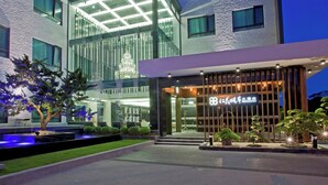 Un hotel moderno con fachada de vidrio, una entrada bien iluminada y un área de jardín ajardinada.