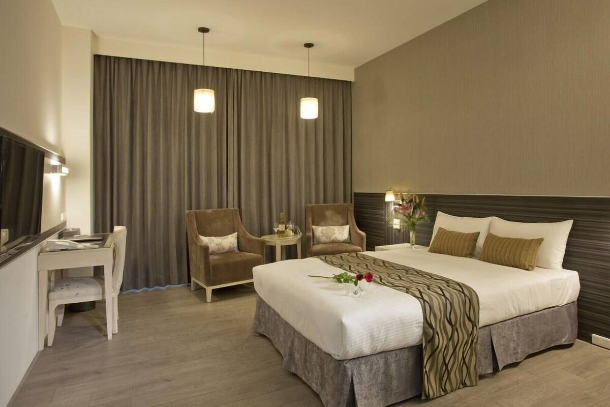 A hotel room with a bed, two chairs, a small table, a TV, and a curtain.